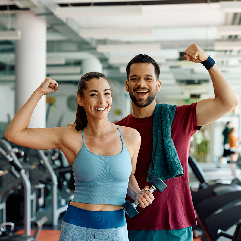 Happy athletic couple flexing their muscles after working out in gym Happy athletic couple flexing their muscles after working out in gym