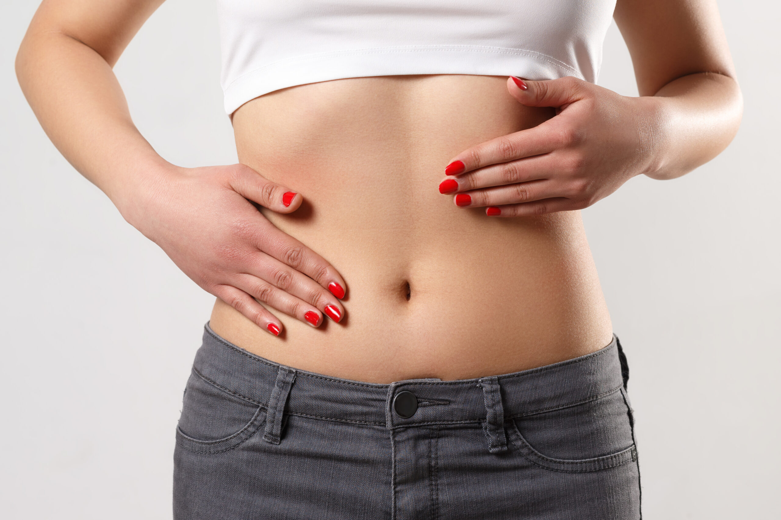 Concept of early term of pregnancy. Close up photo of woman’s abdomen and belly button, she is touching her slim stomach with two hands. isolated white background understanding belly button surgery