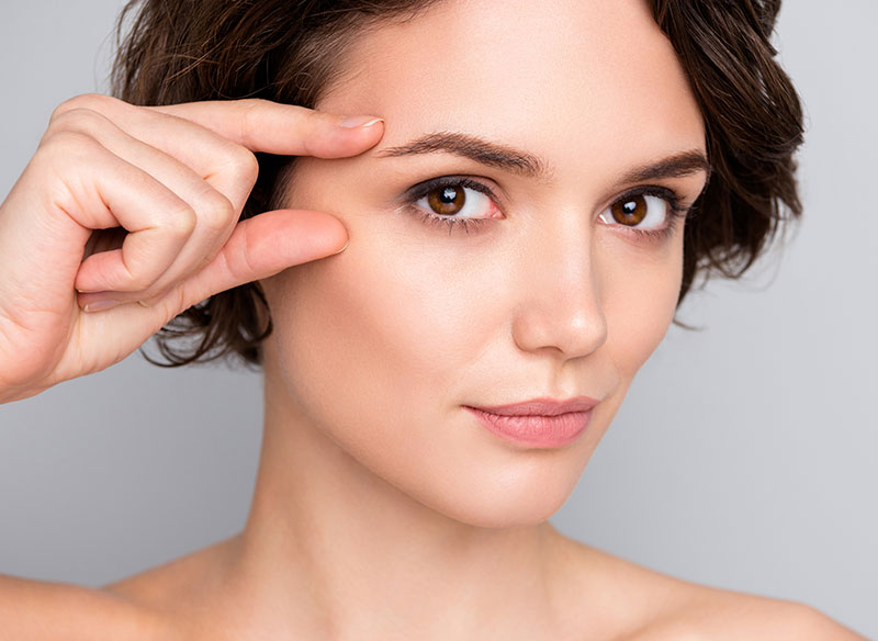 A woman touches her face with her finger, looking at the camera.